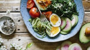 A plate full of healthy dish for ketogenic diets Description: A bowl of vegetables and eggs, suitable for those following ketogenic diets, is placed on a rustic wooden table.