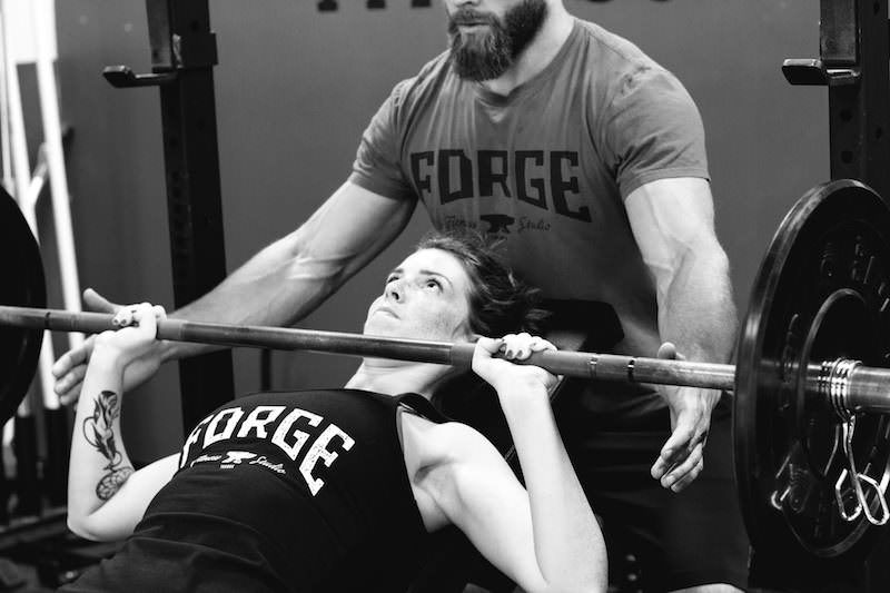 Two individuals engaged in weight training as they perform a bench press exercise in a gym.