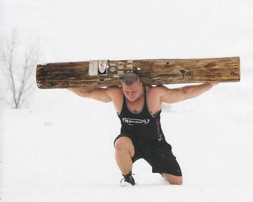 A man lifting a heavy log in the snow, attempting winter weight loss.