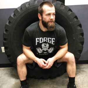 A bearded man sitting on top of a tire.