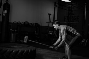 A man doing a tire and sledgehammer workout in a gym.