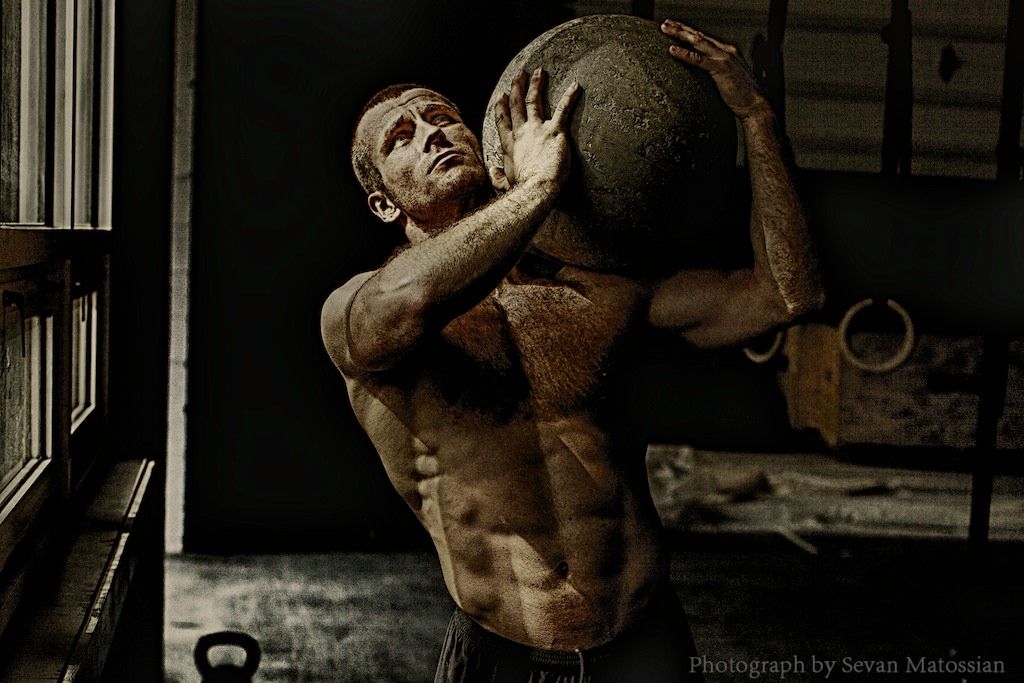 A man undergoing training in a gym, lifting a large ball.