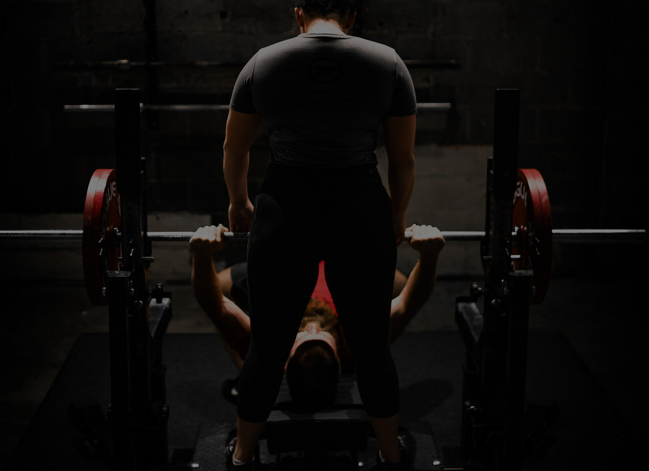 A man doing bench press in a gym with a lady spotter