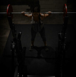 A dark filtered photo of a woman lifting a barbell in a gym.