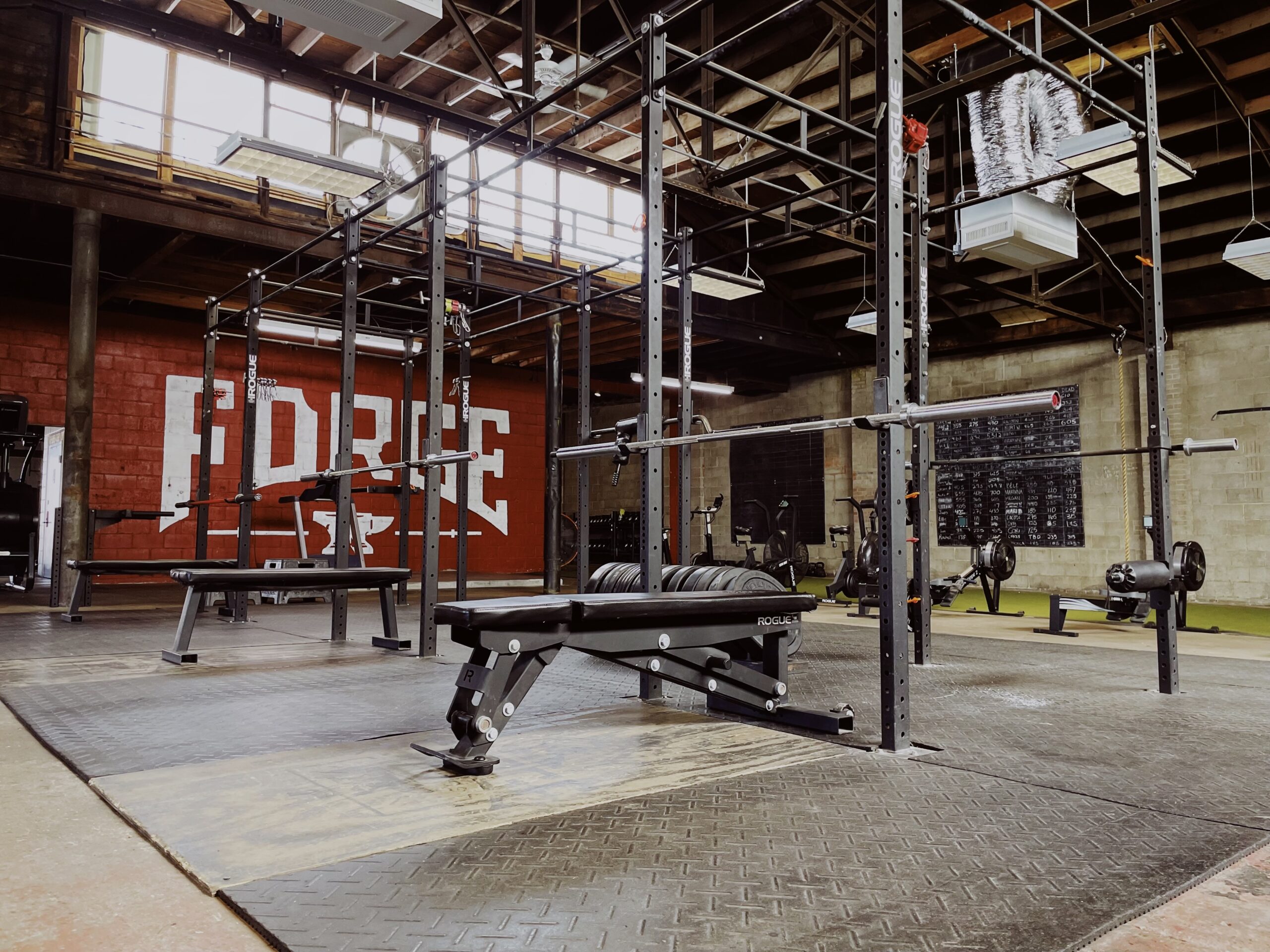 A gym with weights, equipment and a red wall with a painted large logo of Forge Fitness Studio